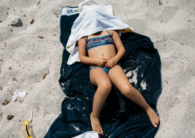 girl in the sun at the beach covering her face with a blue towel